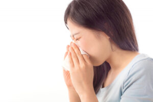 Woman sneezing into a tissue held to her nose, eyes closed
