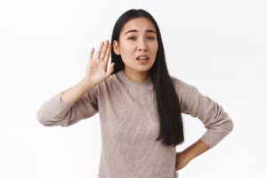Woman with a hand to her ear, listening attentively against a neutral background