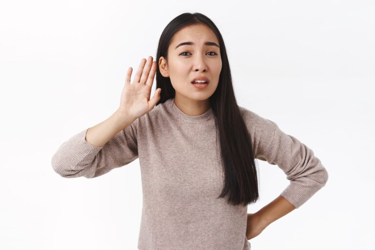 Woman with a hand to her ear, listening attentively against a neutral background