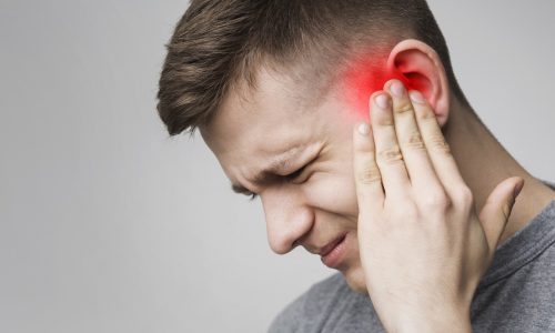 Young man has sore ear, suffering from otitis, touching his inflamed head, close up, empty space